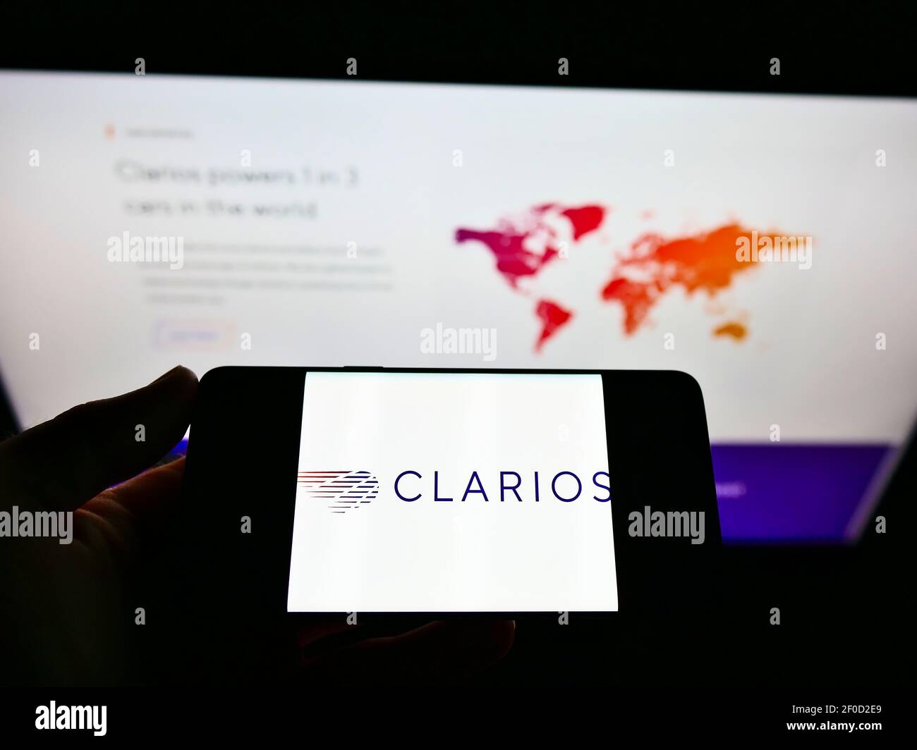 Personne tenant un téléphone portable avec le logo du fabricant américain de batteries Clarios sur l'écran devant le site Web de l'entreprise avec carte. Mise au point sur l'affichage du téléphone. Banque D'Images