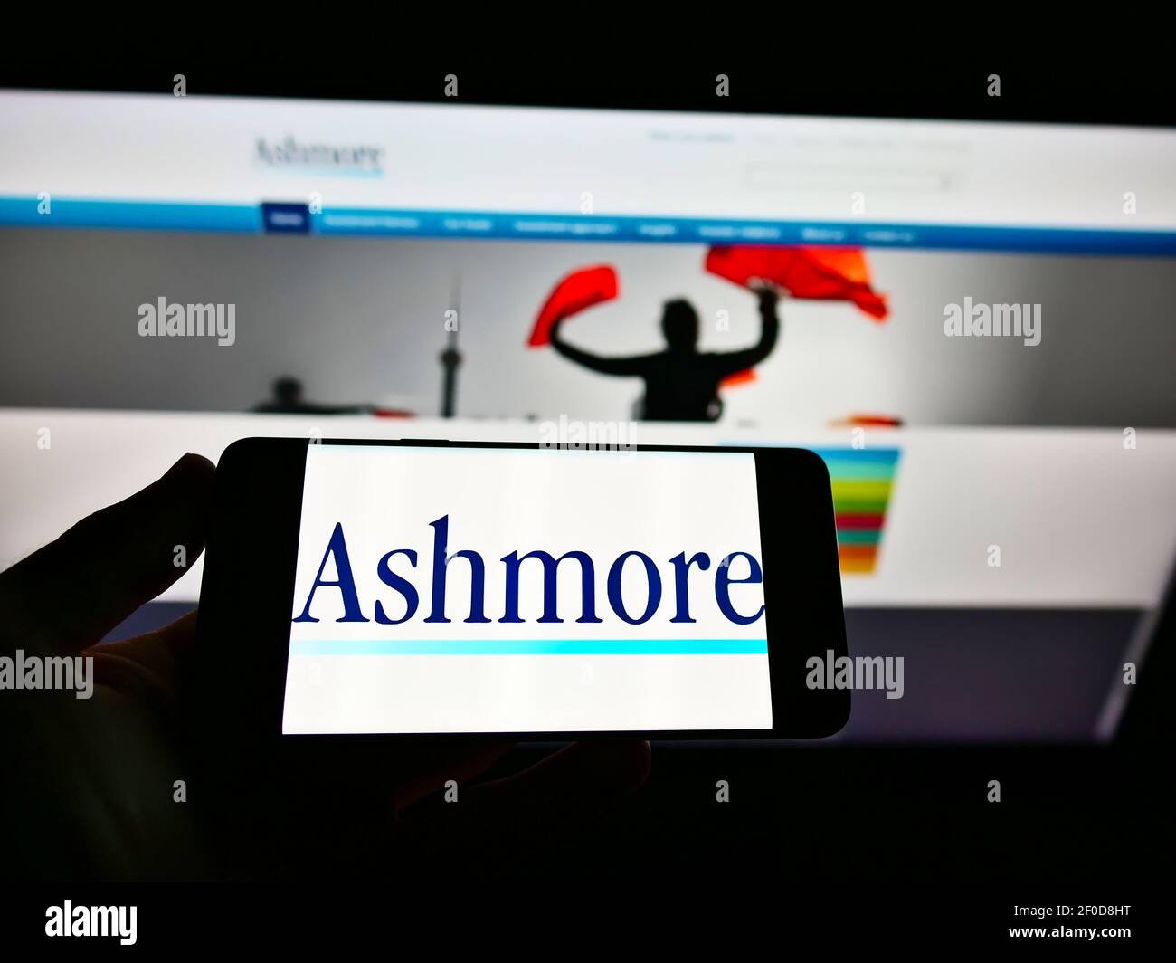 Personne tenant un téléphone portable avec le logo de la société du directeur d'investissement britannique Ashmore Group plc à l'écran en face de la page Web. Mise au point sur l'affichage du téléphone. Banque D'Images