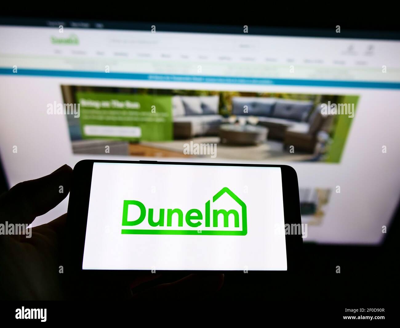 Personne tenant un téléphone portable avec le logo d'affaires du détaillant britannique d'ameublement Dunelm Group à l'écran en face de la page Web. Mise au point sur l'affichage du téléphone. Banque D'Images