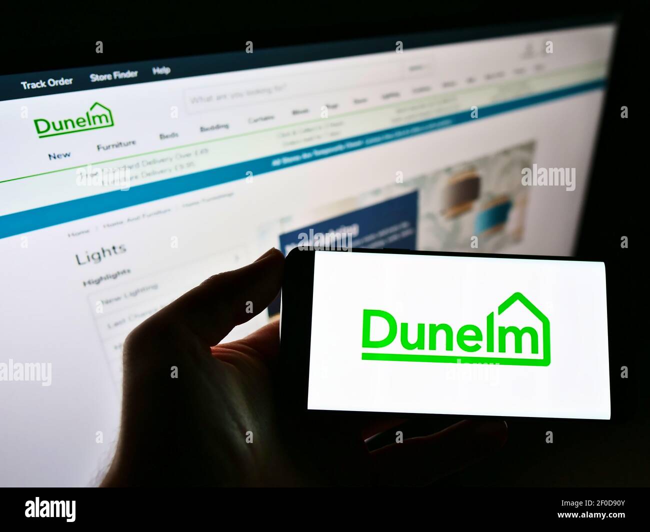 Personne tenant un smartphone avec le logo du détaillant britannique Dunelm (Soft Furnishings) Limited à l'écran devant le site Web. Mise au point sur l'affichage du téléphone. Banque D'Images