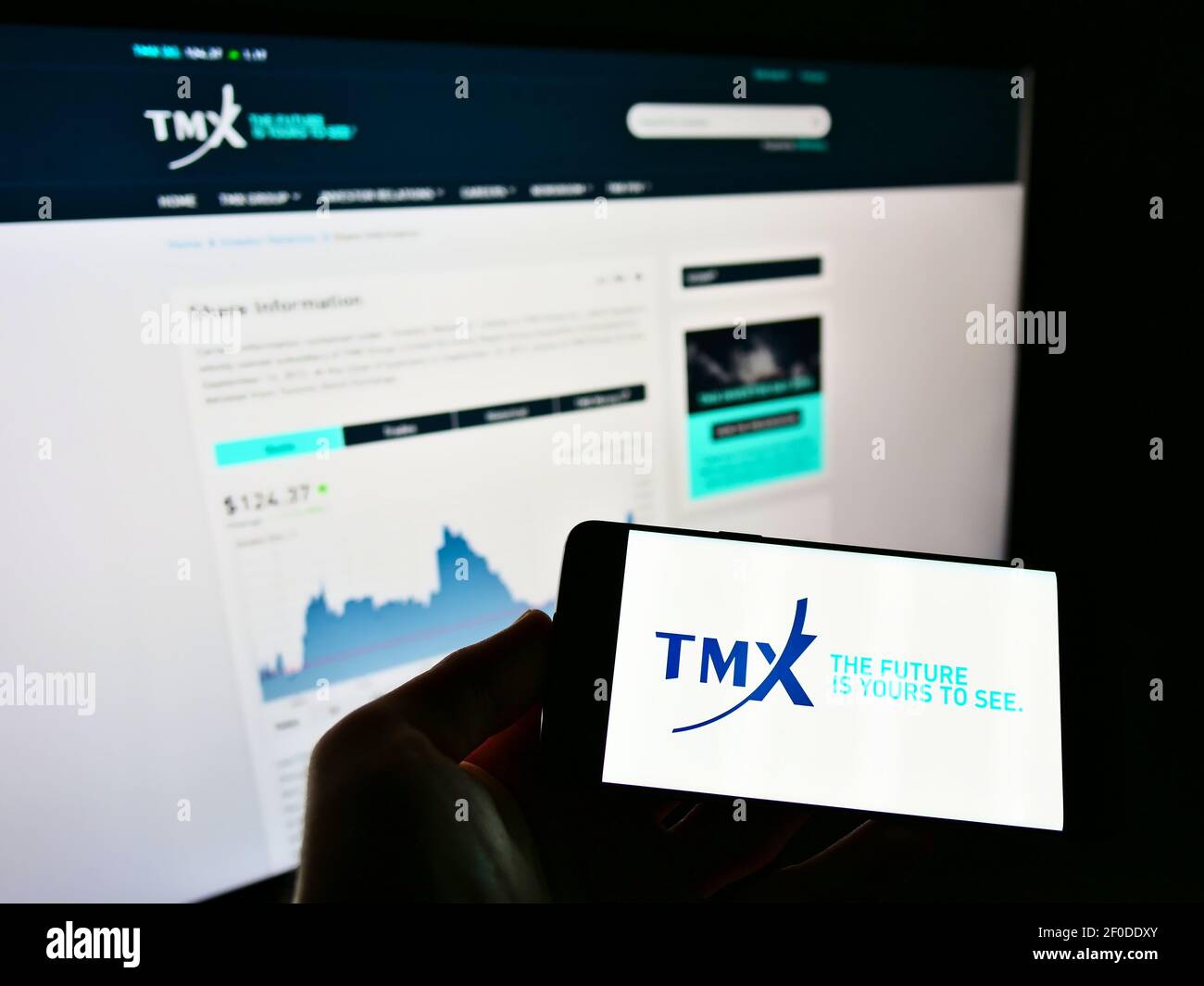 Personne tenant un téléphone portable avec le logo de la société canadienne de services financiers TMX Group Limited à l'écran devant la page Web. Mise au point sur l'affichage du téléphone. Banque D'Images