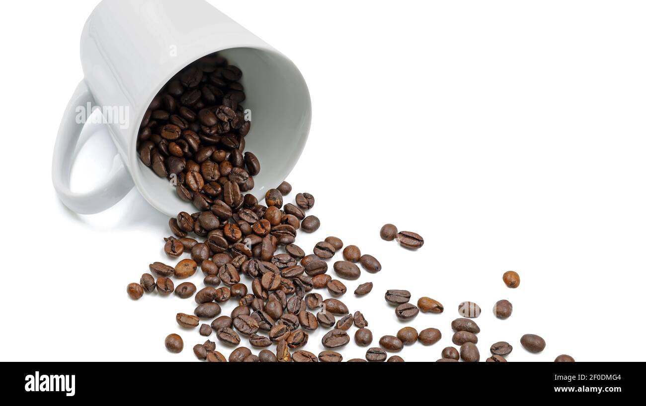 Les grains de café torréfiés tombent d'une tasse de café couchée isolée sur fond blanc Banque D'Images