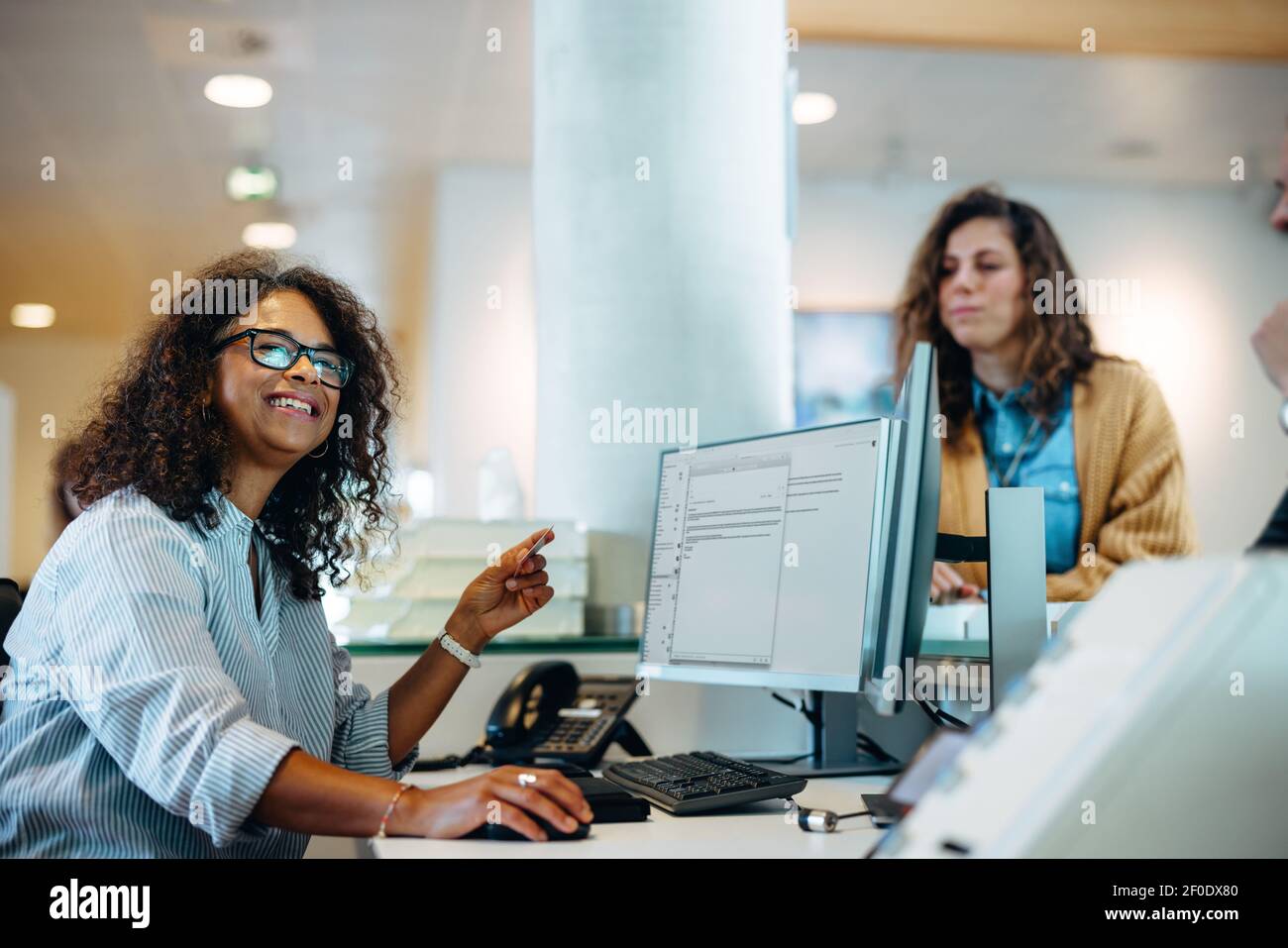 Femme travaillant à la réception du bureau du gouvernement qui regarde loin et souriait avec des gens qui font la queue à la réception. Banque D'Images