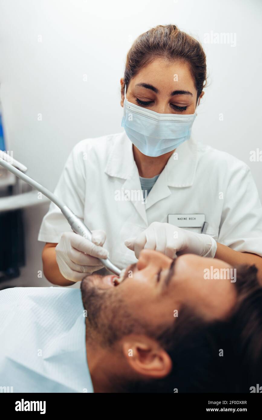 Femme médecin traitant les dents de l'homme dans le fauteuil du dentiste. Femme dentiste portant un masque facial traitant un patient. Banque D'Images