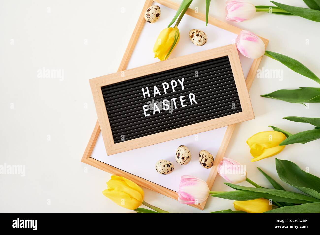 Bouquet de tulipes de printemps, œufs de caille et planche avec inscription Joyeuses Pâques. Concept de ressort Banque D'Images