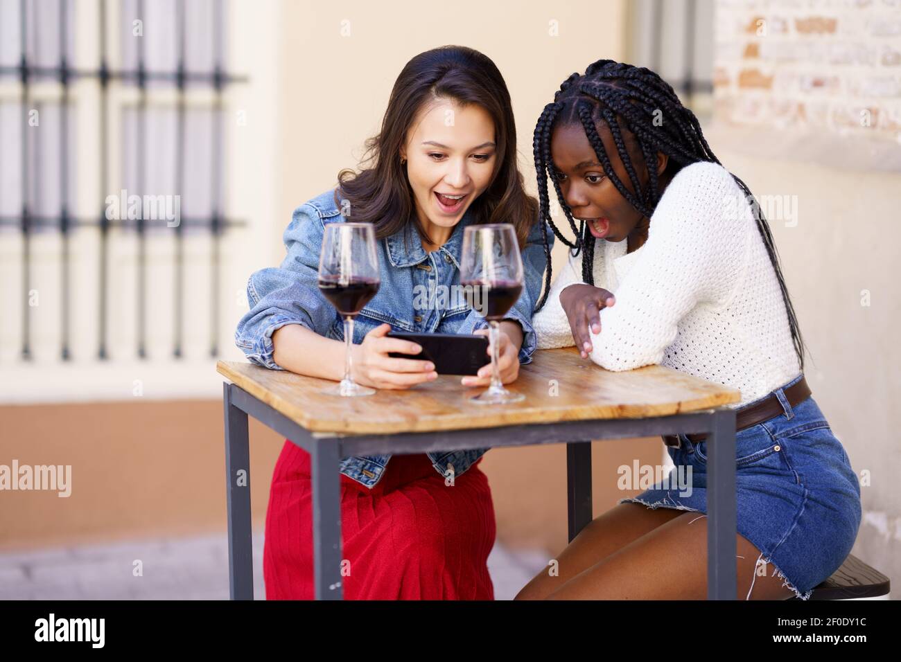 Deux femmes regardant leur smartphone ensemble tout en ayant un verre de vin. Banque D'Images