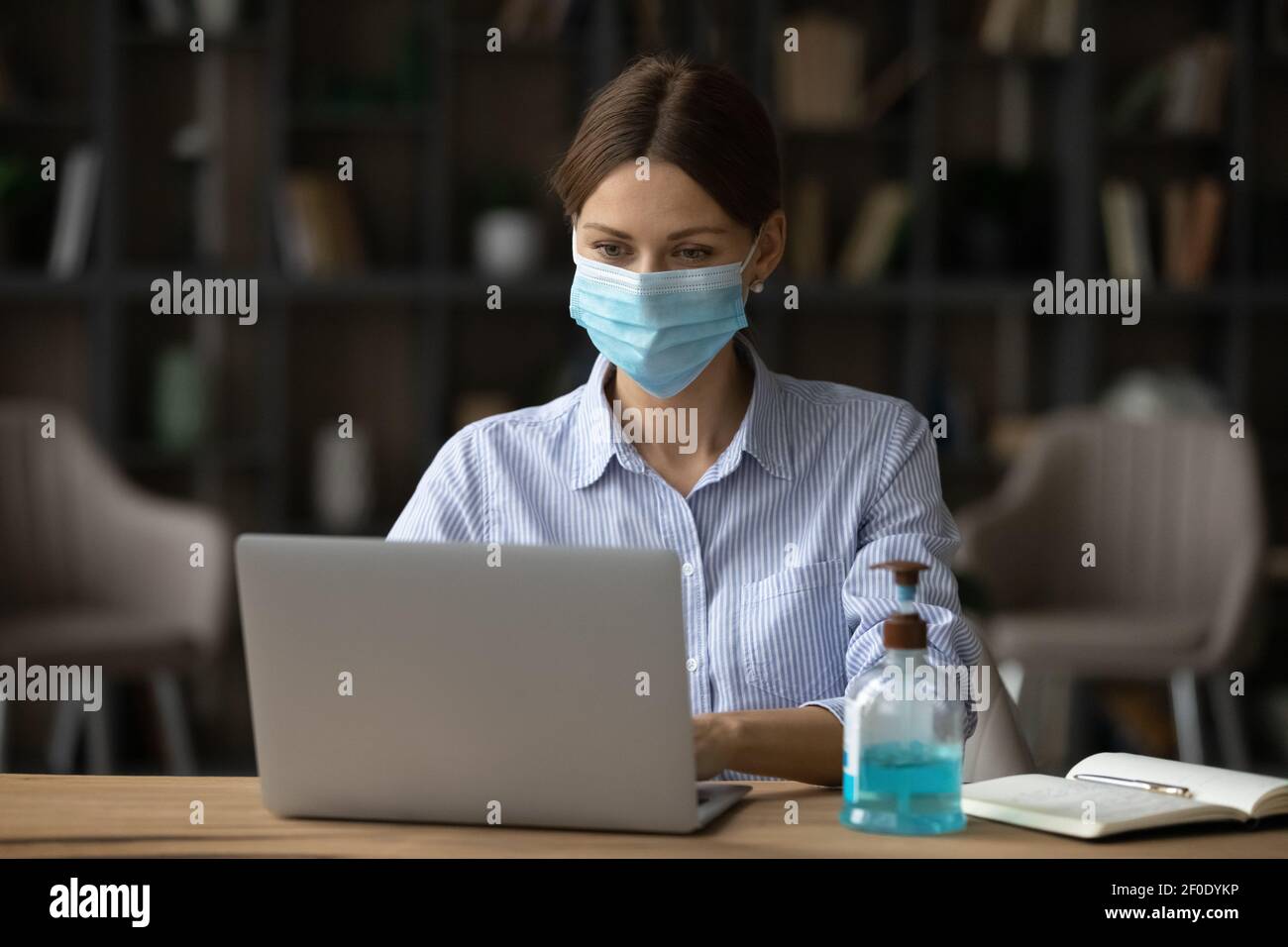 Une femme d'affaires caucasienne porte un masque de visage sur un ordinateur portable Banque D'Images