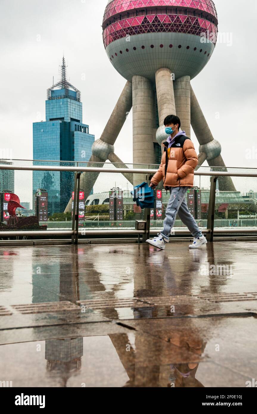 Un jeune homme sur la passerelle devant la tour de perle orientale à Lujiazui, dans le district de Pudong, en Chine, lors d'une journée froide et pluvieuse au début du printemps. Banque D'Images