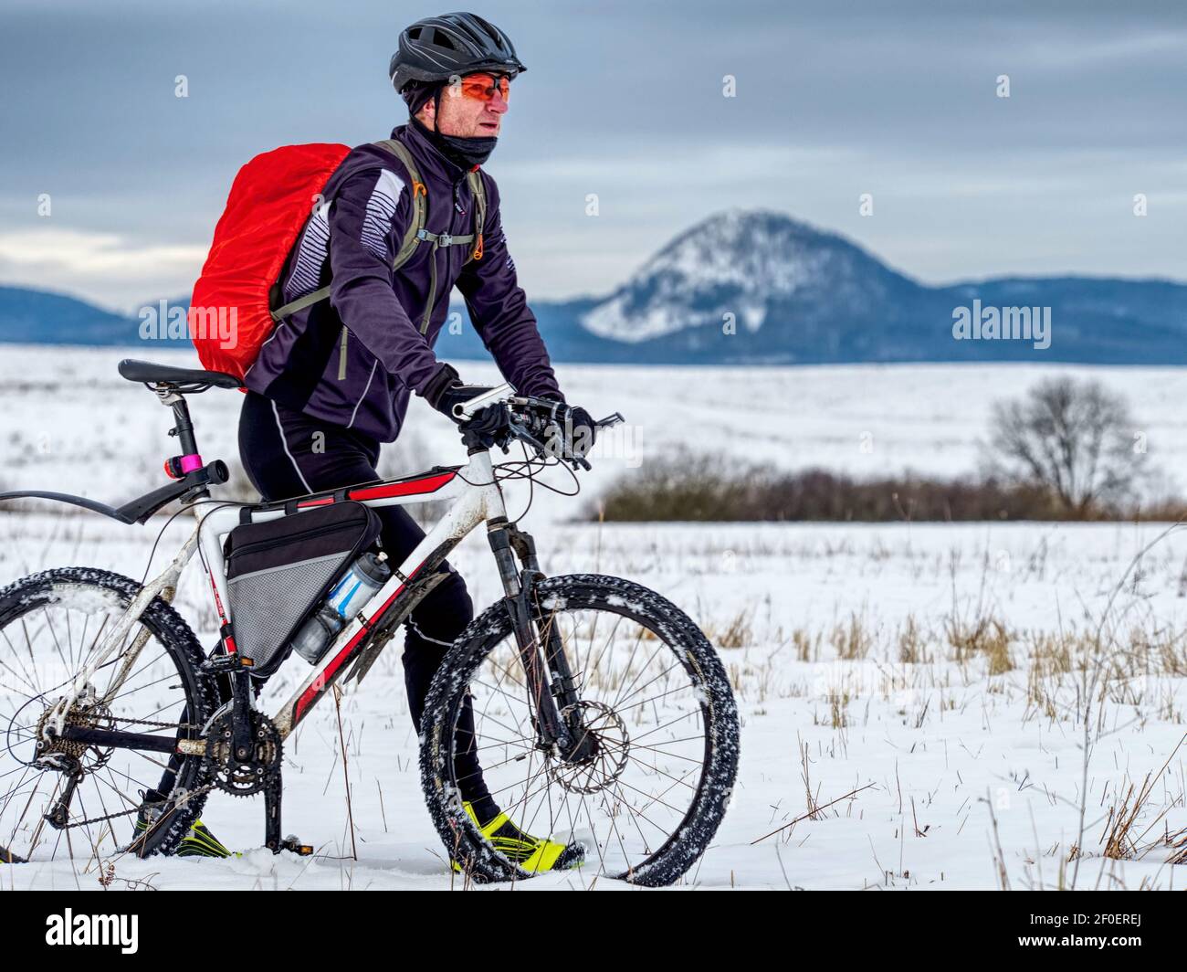 Cycliste en costume de sport noir poussant le vélo de montagne sur la piste de neige. Sports d'hiver extrêmes et concept Enduro Motos. Banque D'Images