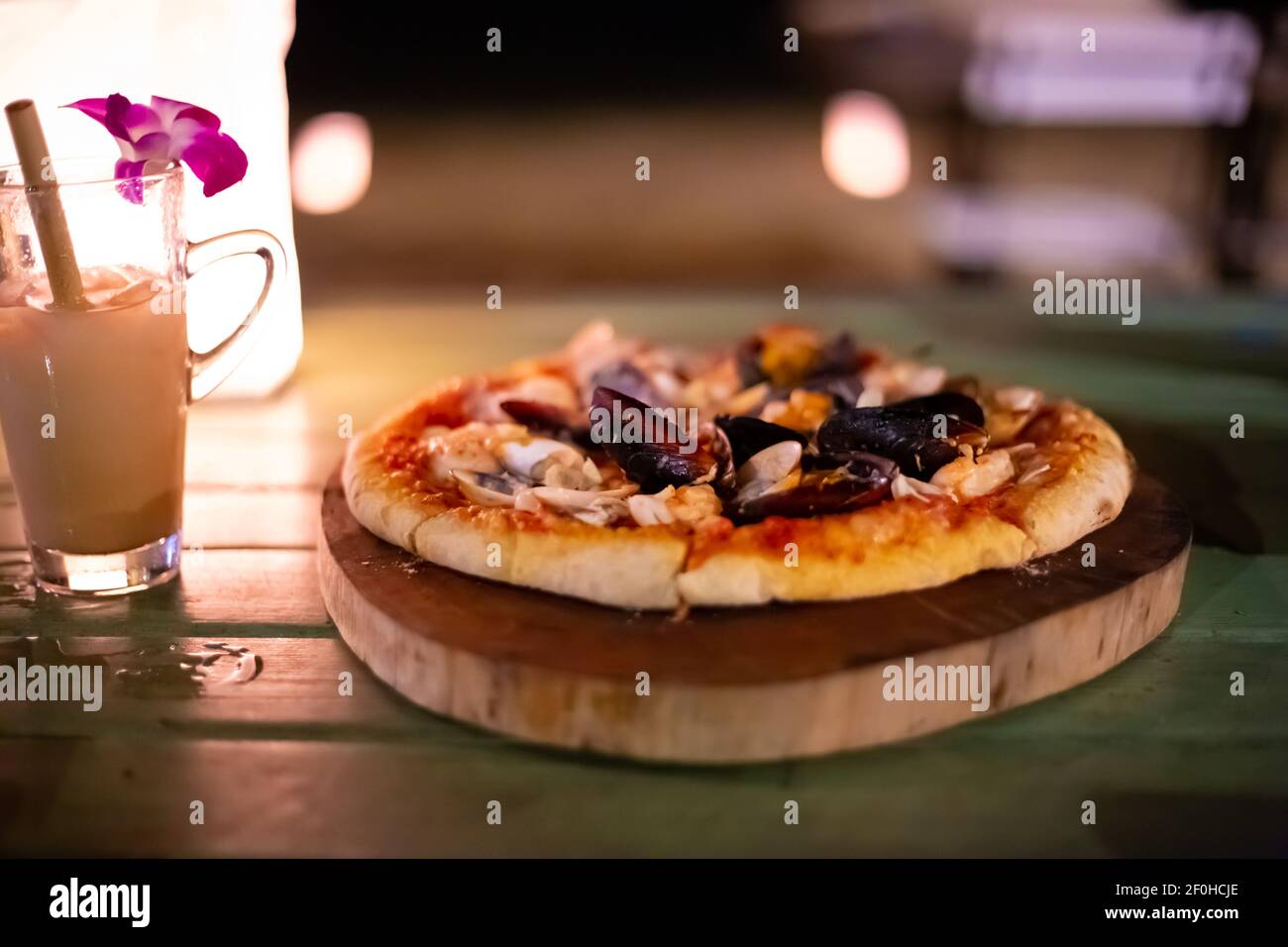 pizza avec fruits de mer sur une table dans un café, à côté d'un cocktail avec une fleur d'orchidée, un délicieux dîner sur la mer, fond flou Banque D'Images