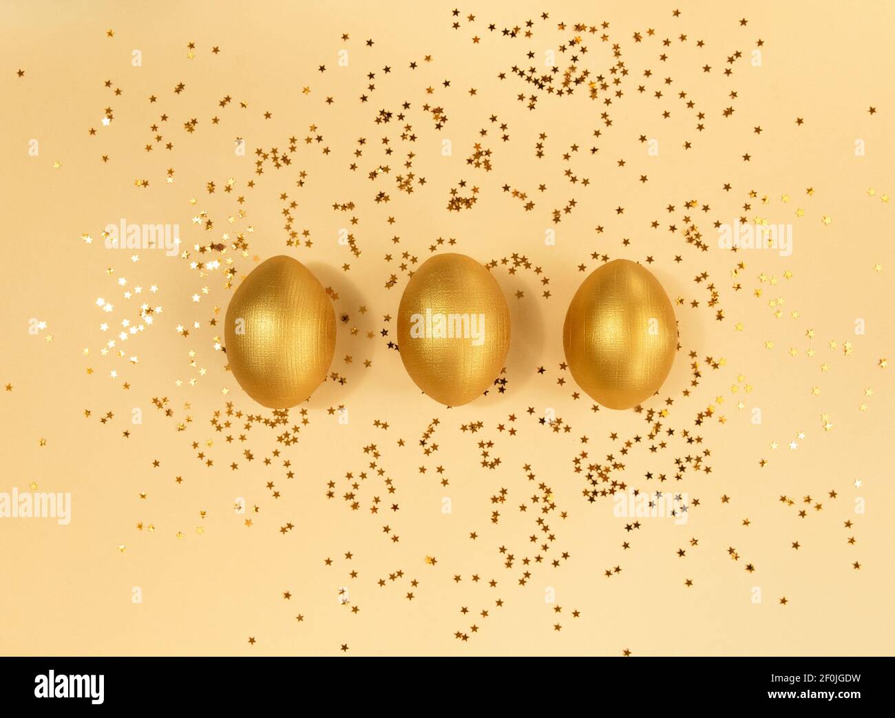 Trois œufs et confettis dorés en bois de pâques sur fond beige. Banque D'Images