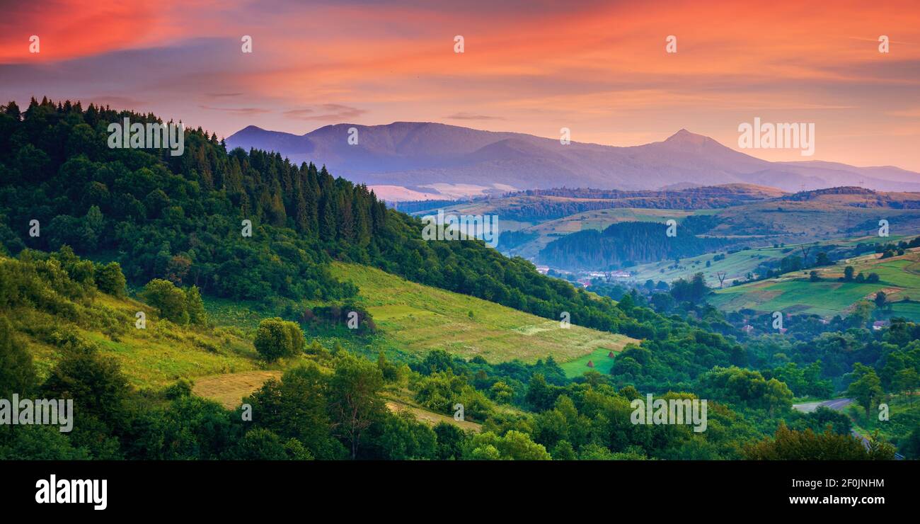 paysage rural montagneux à l'aube. beau paysage avec des forêts, des collines et des prairies dans la lumière du matin. crête à pic élevé au loin. village Banque D'Images