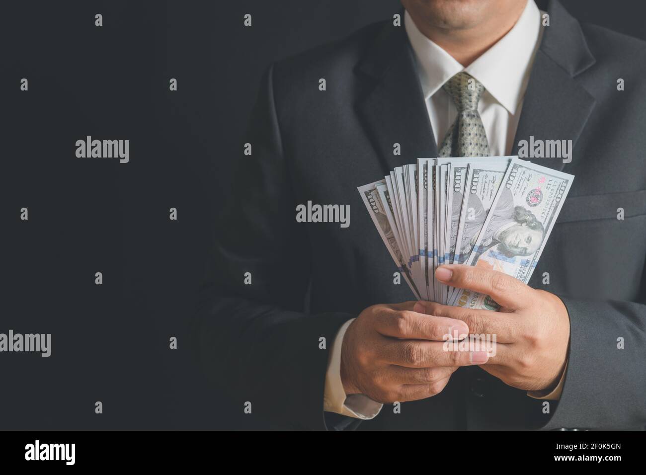 Homme d'affaires portant un costume et une cravate tenant de l'argent à la main sur fond noir, des billets en dollars américains (USD) - investissement, succès et affaires rentables c Banque D'Images
