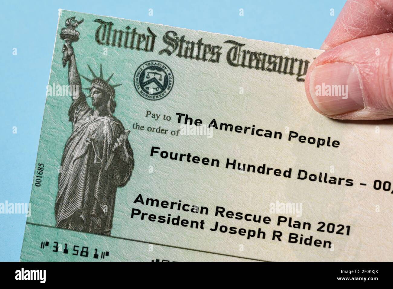 Tenir un chèque-exemple du Trésor américain pour illustrer l'Amérique Plan de sauvetage Act de 2021 paiement sur fond bleu Banque D'Images