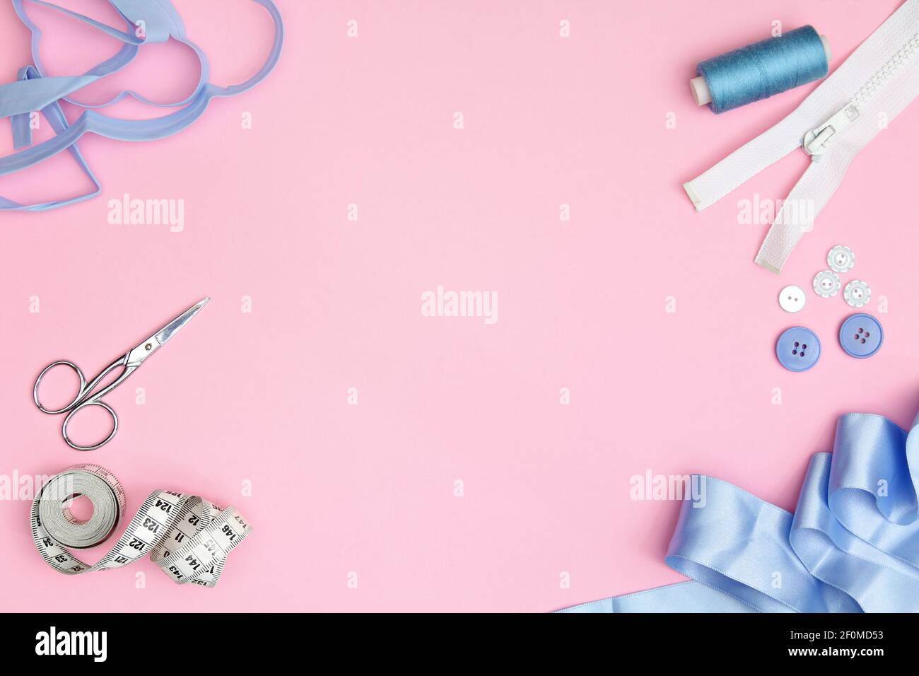 Accessoires de couture sur fond rose avec aiguilles, bobine de fil, ciseaux et mètre à ruban Banque D'Images