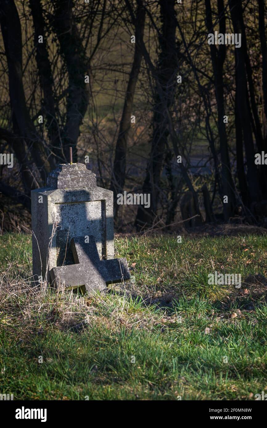 Ancienne pierre tombale avec croix brisée mais avec une ombre en forme de croix sous les arbres dans un cimetière abandonné, symbole religieux, espace de copie, foyer choisi Banque D'Images