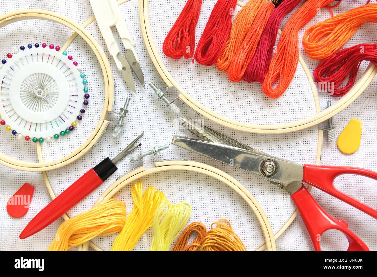 Accessoires de broderie sur toile de lin blanche. Cerceau à broderie, fils, aiguille et ciseaux. Couleur rouge et jaune Banque D'Images