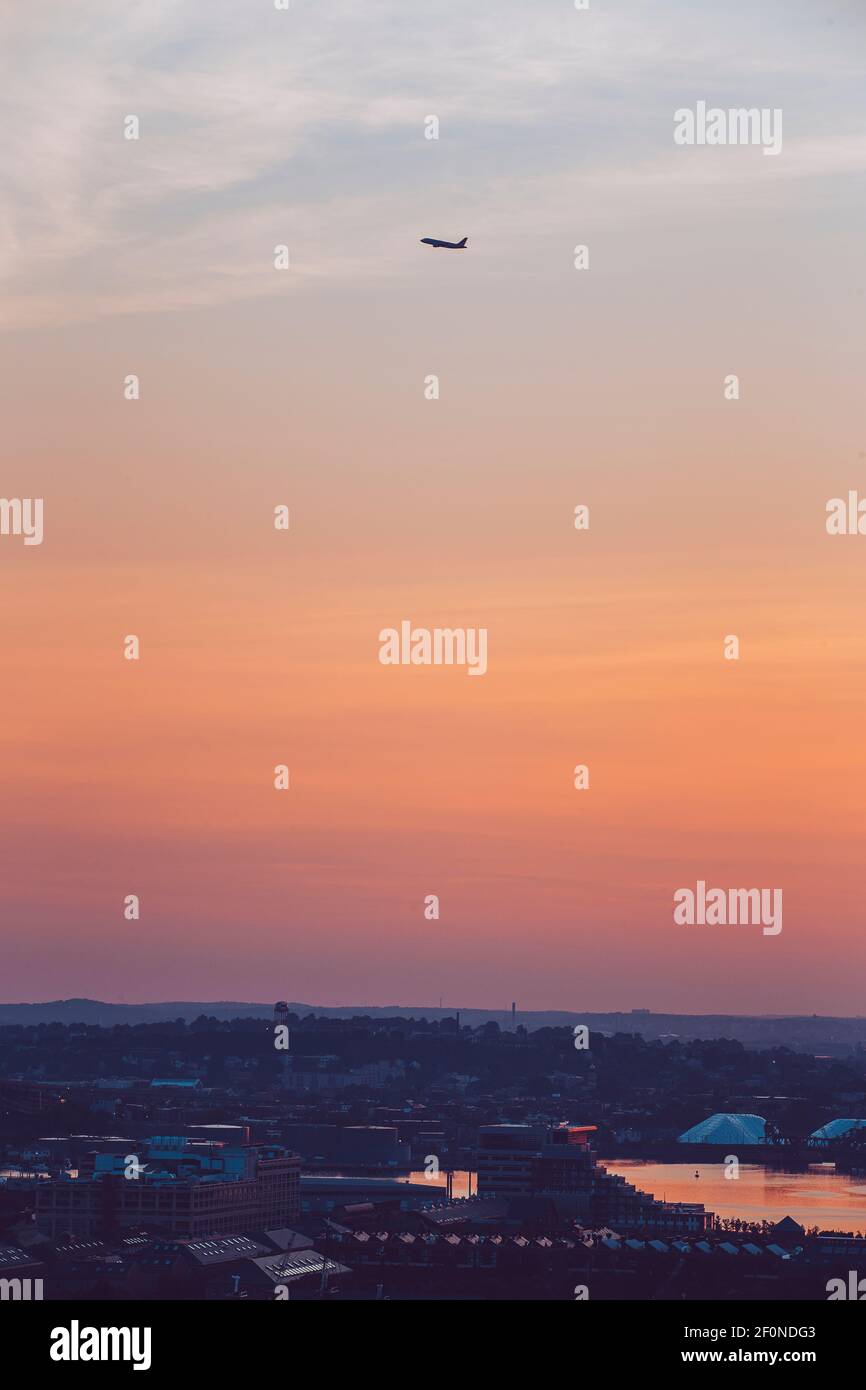 Un avion prend le dessus de la ville de Boston, ma pendant le lever du soleil. Banque D'Images