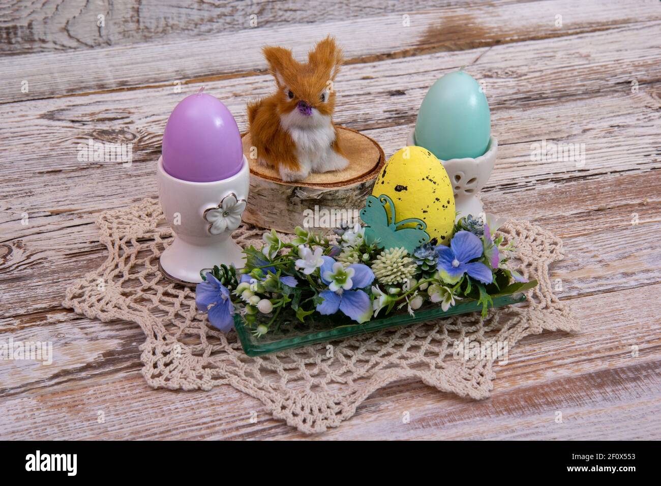 Lapin de Pâques sur une souche avec des fleurs d'oeufs de Pâques et des bougies en forme d'oeufs. Banque D'Images