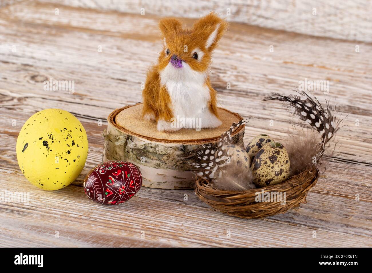 Lapin de Pâques sur une souche avec des oeufs de Pâques dans un panier avec des plumes. Banque D'Images