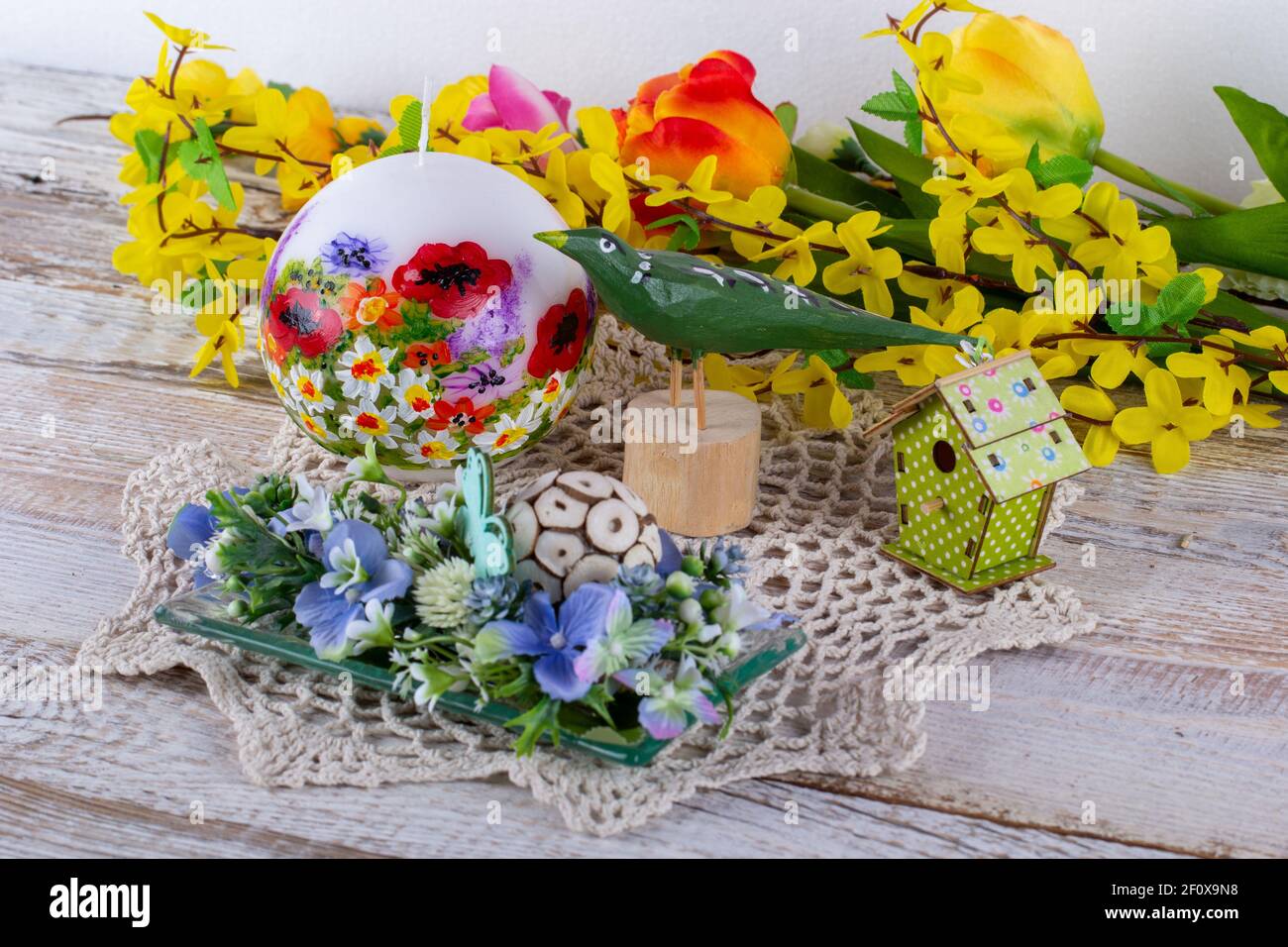 Un arrangement de printemps de fleurs avec une bougie, un oiseau en bois et un birdhouse. Banque D'Images