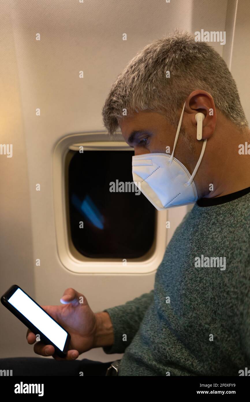 Homme avec un smartphone, des écouteurs et un masque dans la cabine d'un avion. Concept de voyage Banque D'Images