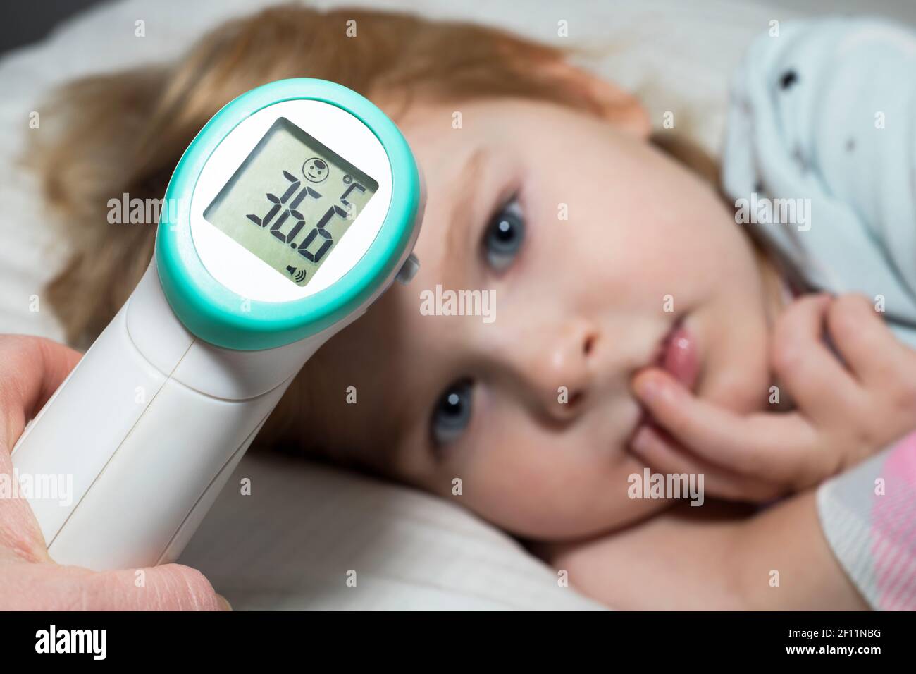 Prendre la température d'un petit enfant, allongé dans le lit. Un parent mesure la température de son enfant à l'aide d'un thermomètre sans contact pendant l'épidémie de coronavirus. Banque D'Images