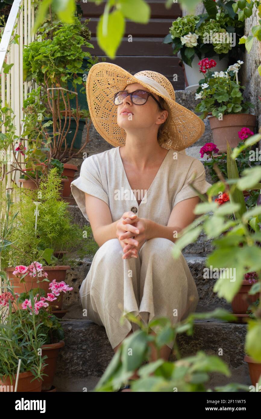 Belle touriste femme portant un grand chapeau de paille et un short assis et  reposant sur les escaliers de la maison en pierre ancienne pendant les  voyages d'été sur la Méditerranée Photo