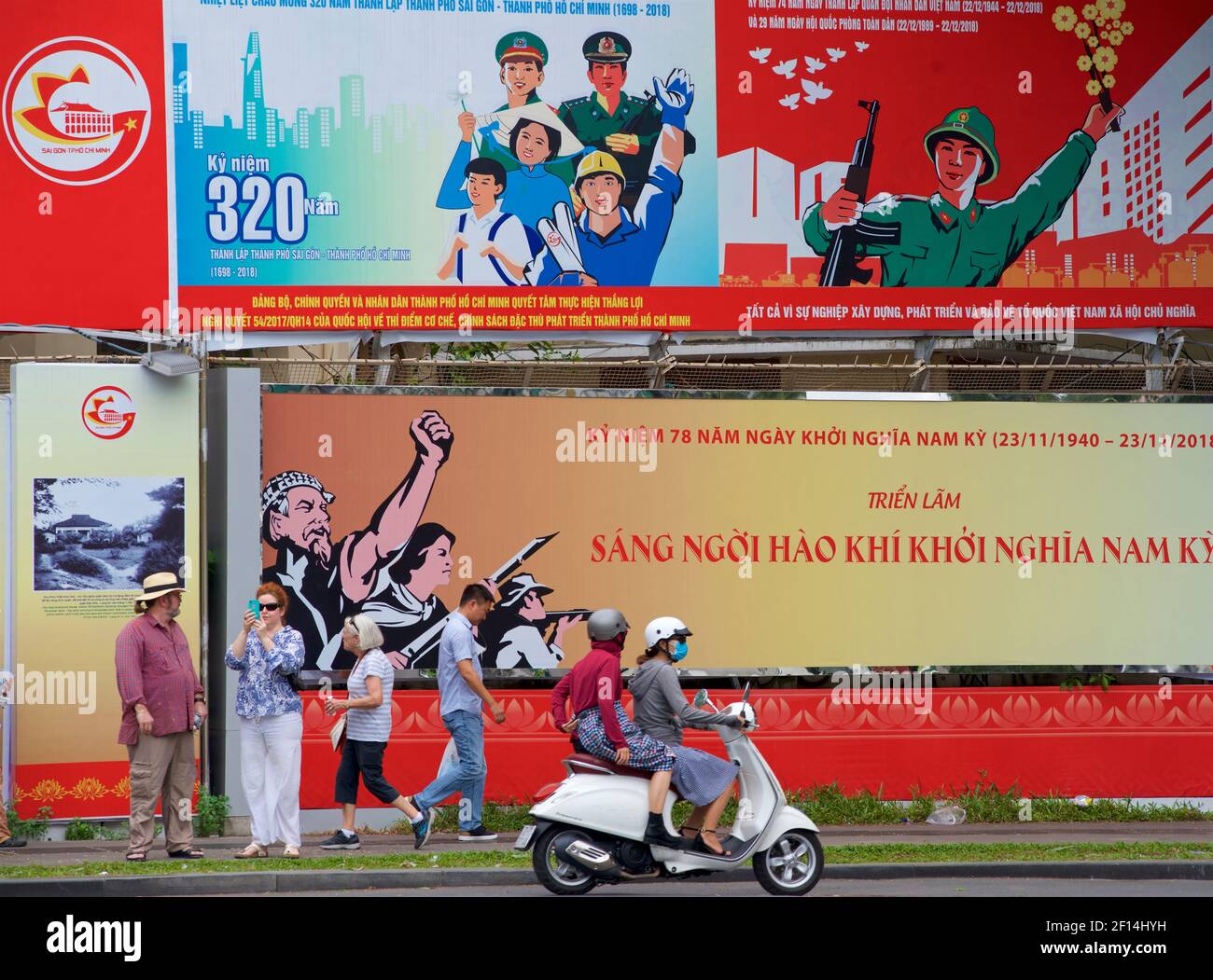 Panneaux d'affichage socialistes érigés dans le réseau Ho Chi Minh ville, Vietnam. Touristes, piétons, et une moto de passage. Banque D'Images