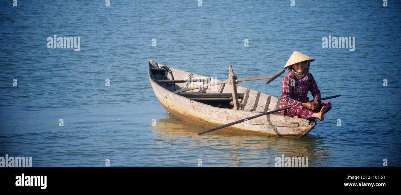Femme vietnamienne en chapeau conique distinctif dans un petit bateau sur la rivière Thu bon, Hoi an, Vietnam. Banque D'Images