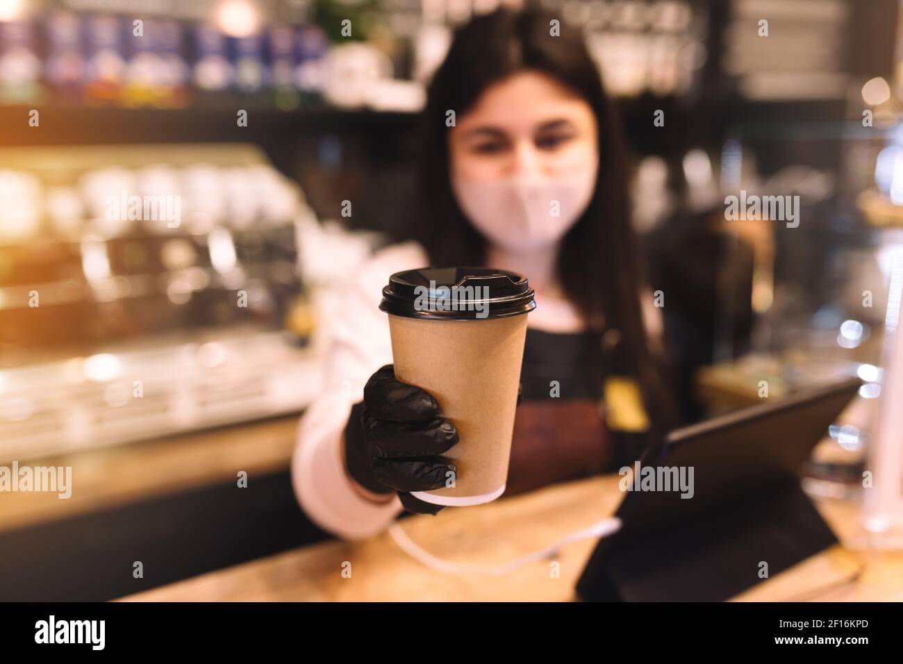 Le Barista en masque de protection et gants noirs donne une tasse de café dans le café. Photo de haute qualité Banque D'Images