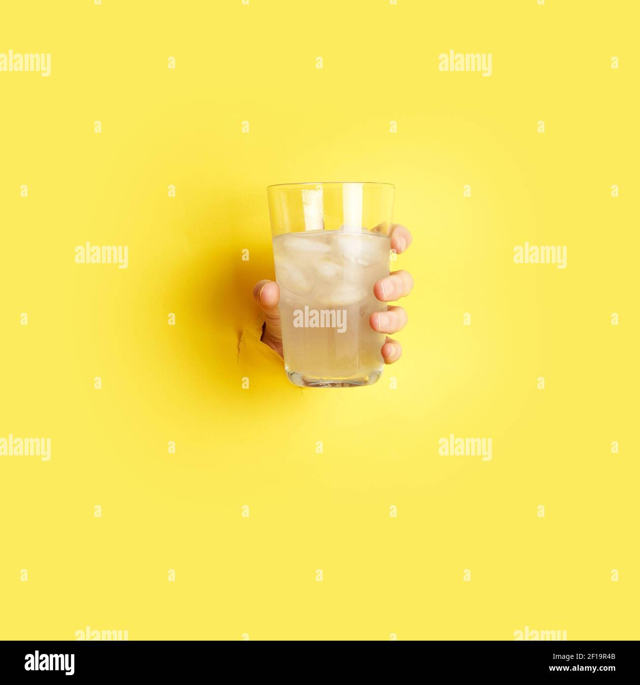 femme main tenant le verre avec la limonade à travers le trou dans papier jaune Banque D'Images