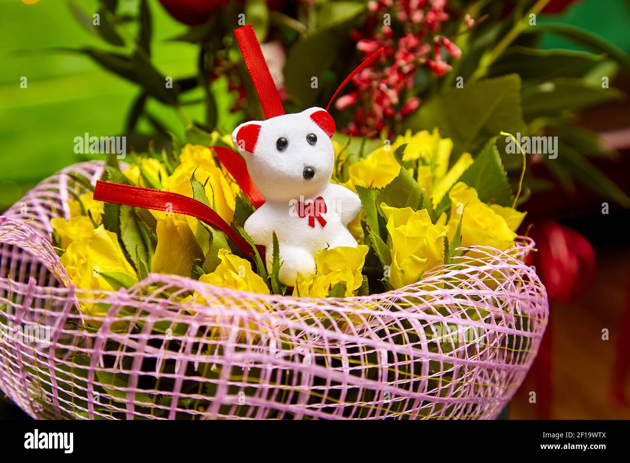 Ours blanc en peluche portant des fleurs roses jaunes Banque D'Images