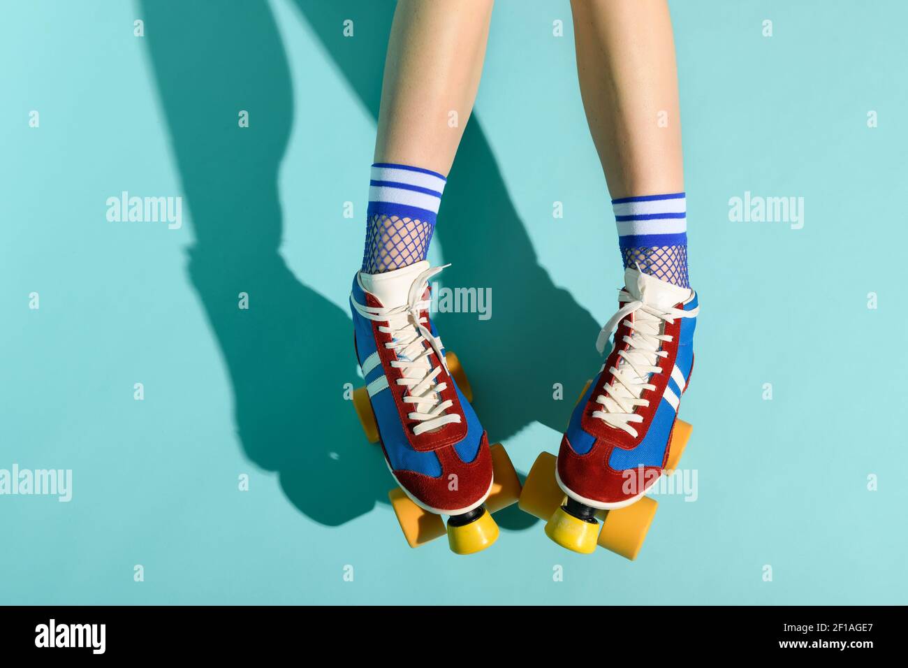 Vue en haut et en bas des pieds et de la jambe inférieure de une femme portant des rollerskates rouges et bleus avec des roues jaunes sur fond bleu avec espace de copie et mode Banque D'Images