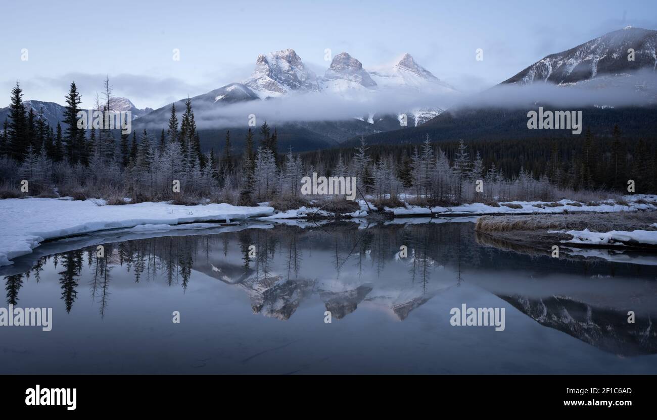 Photo d'hiver avant le lever du soleil des Rocheuses canadiennes avec la montagne reflétée dans l'eau, prise à Three Sisters Mountain, Canmore, Alberta, Canada Banque D'Images