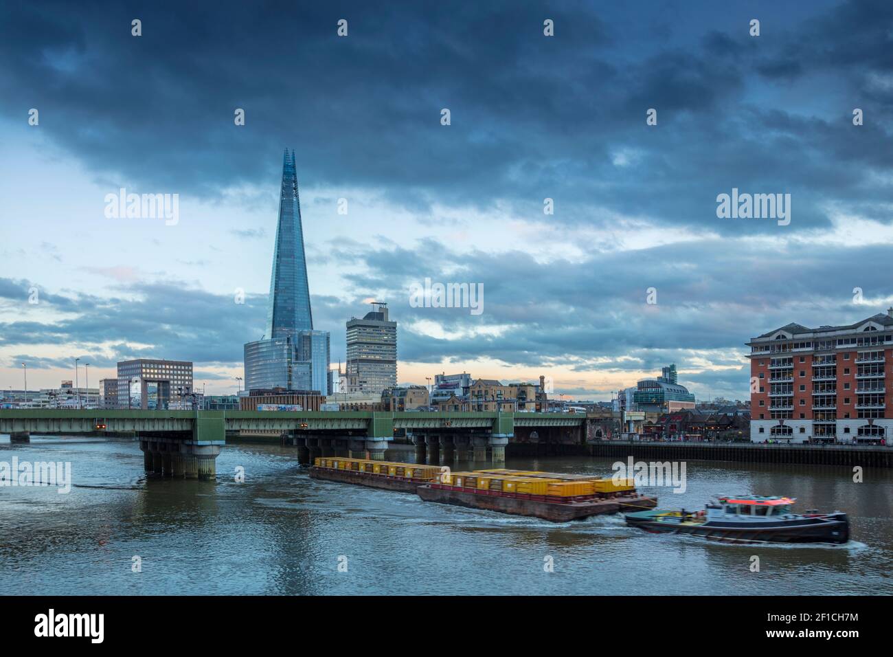 Une barge fluviale qui déplace des conteneurs contenant des déchets comme fret sur la voie navigable de la Tamise, le pont de Cannon Street, la ligne d'horizon du centre de Londres, au Royaume-Uni Banque D'Images