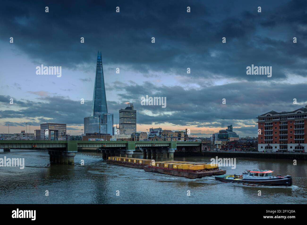 Une barge fluviale qui déplace des conteneurs contenant des déchets comme fret sur la voie navigable de la Tamise, le pont de Cannon Street, la ligne d'horizon du centre de Londres, au Royaume-Uni Banque D'Images