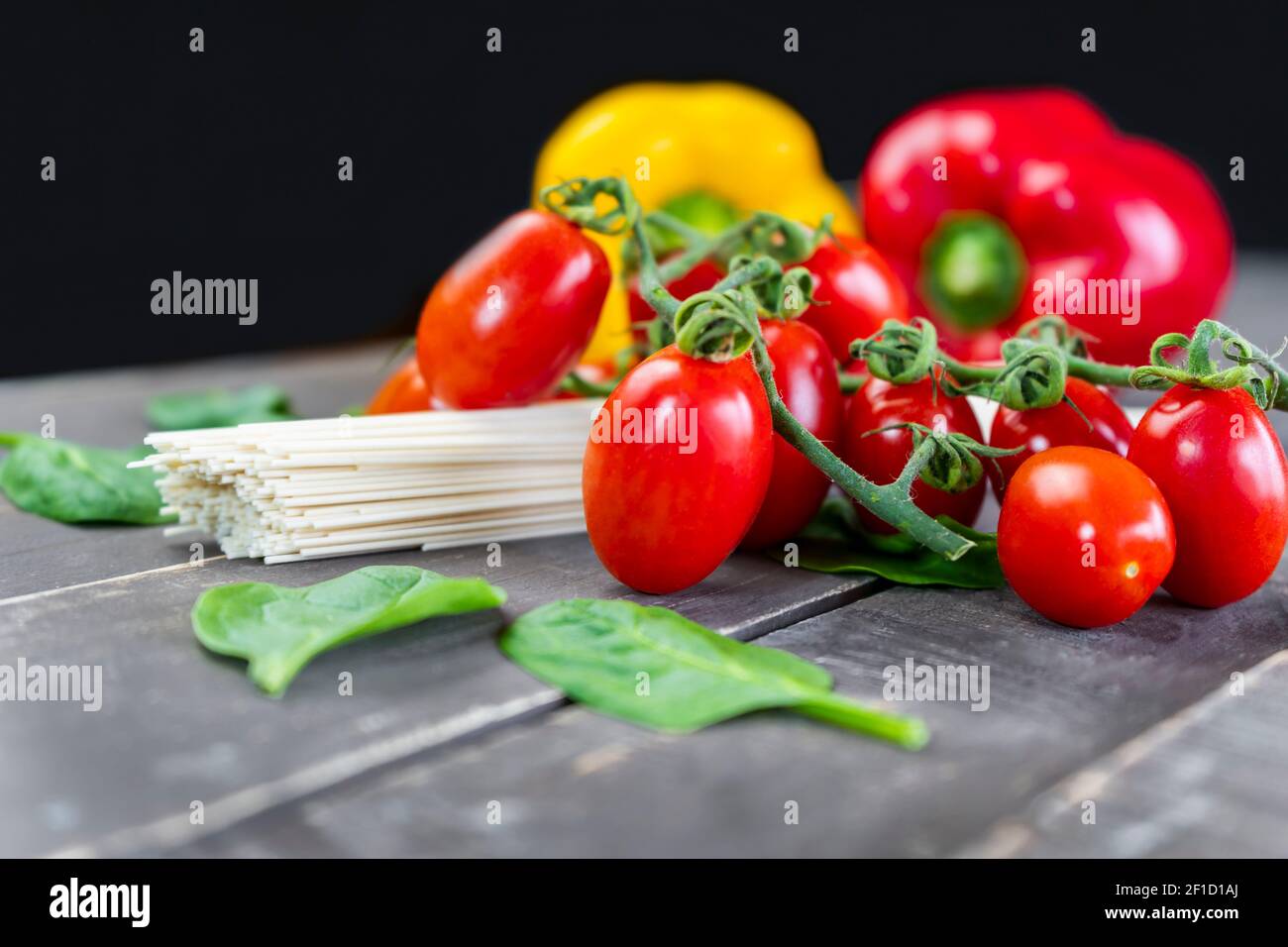 Vue rapprochée de légumes frais biologiques avec pâtes crues sur table en bois.tomates cerises, feuilles d'épinards et poivrons colorés sur fond sombre. Banque D'Images