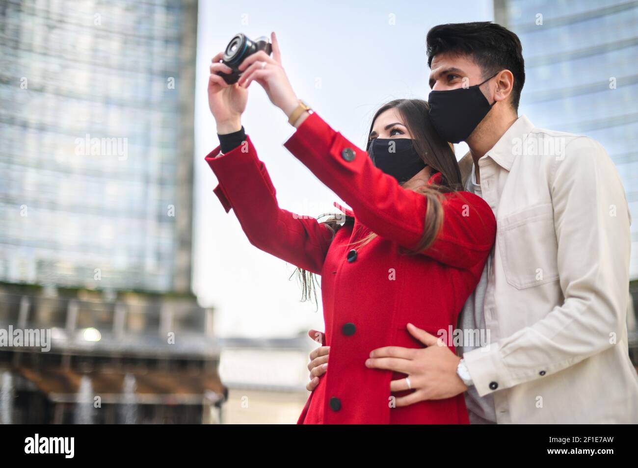 Les touristes heureux avec des masques covid ou coronavirus couple whalking ensemble dans une ville et photographier un endroit intéressant Banque D'Images