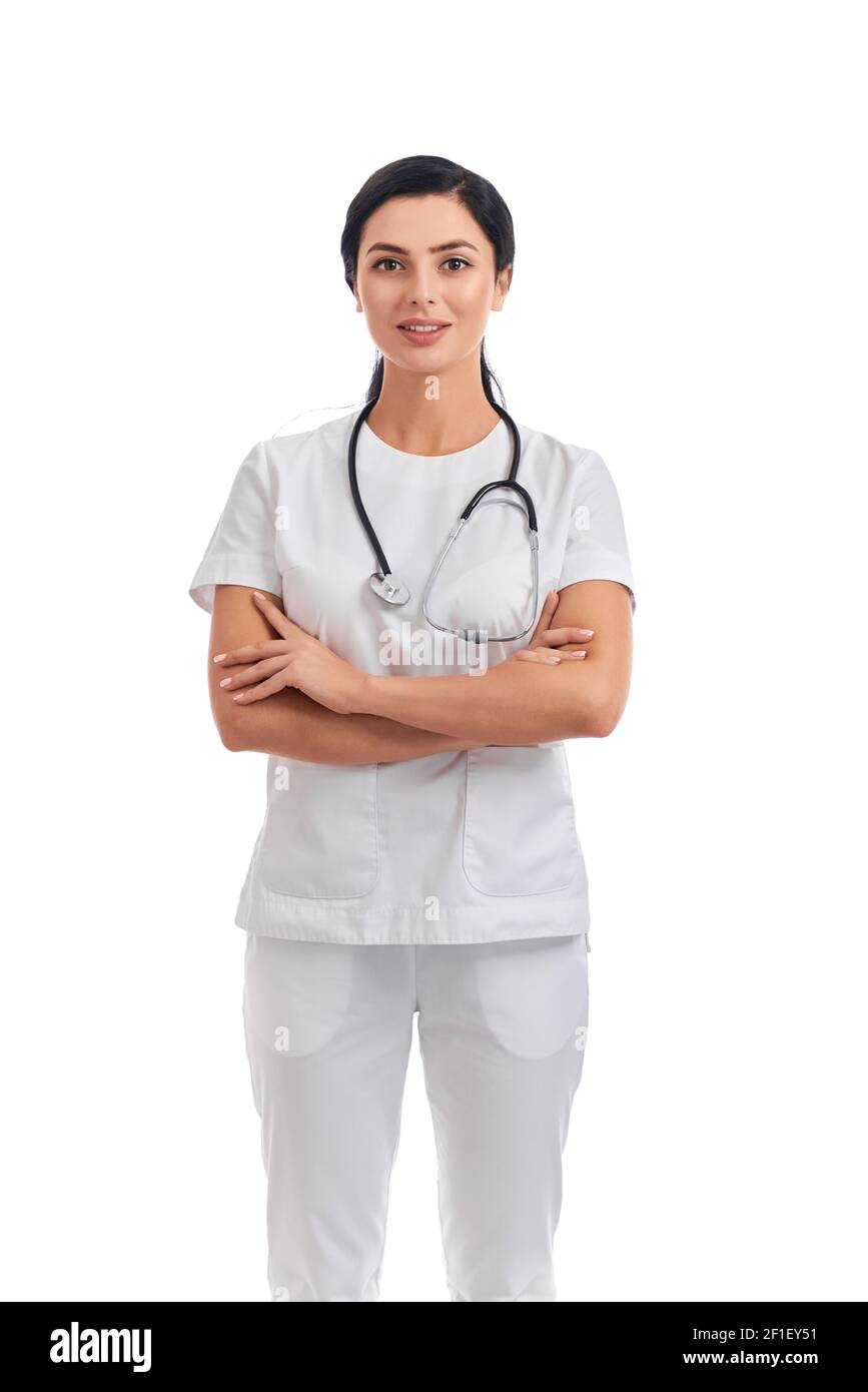 Charmante femme médecin en uniforme médical avec stéthoscope sur le cou debout sur fond blanc et main de retenue croisée. Concept de soins de santé. Banque D'Images