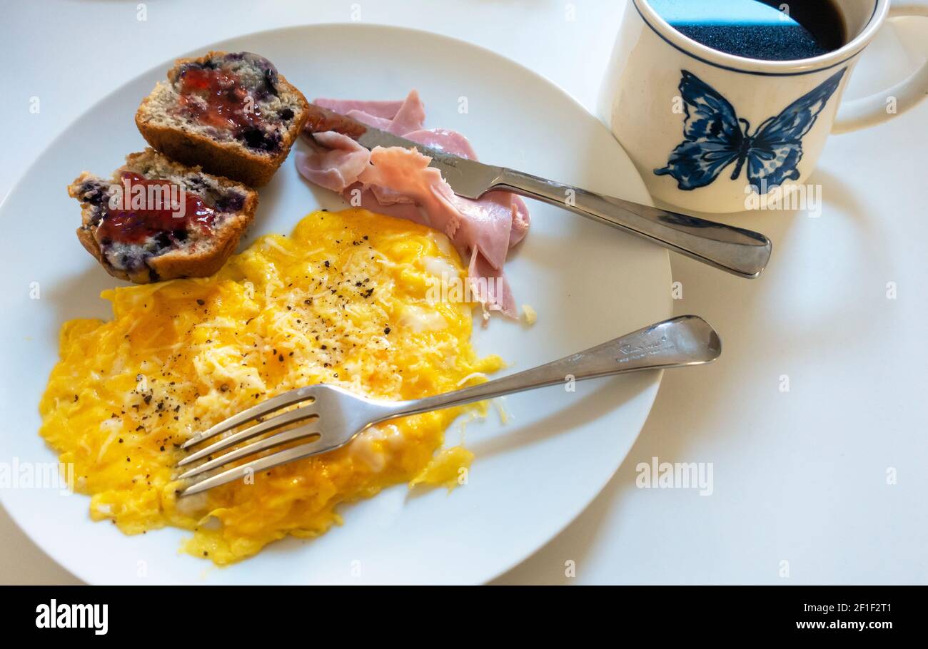 Œufs brouillés au jambon, fromage râpé, muffin aux myrtilles et une tasse de café noir Banque D'Images