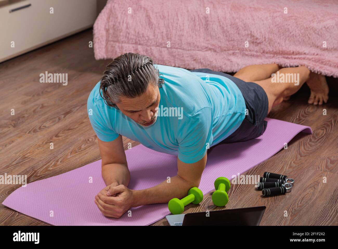 l'homme de 50 ans effectue des exercices tout en étant allongé sur le tapis à la maison, en regardant l'ordinateur. En cas de pandémie, une personne s'entraîne dans un appartement via le Banque D'Images