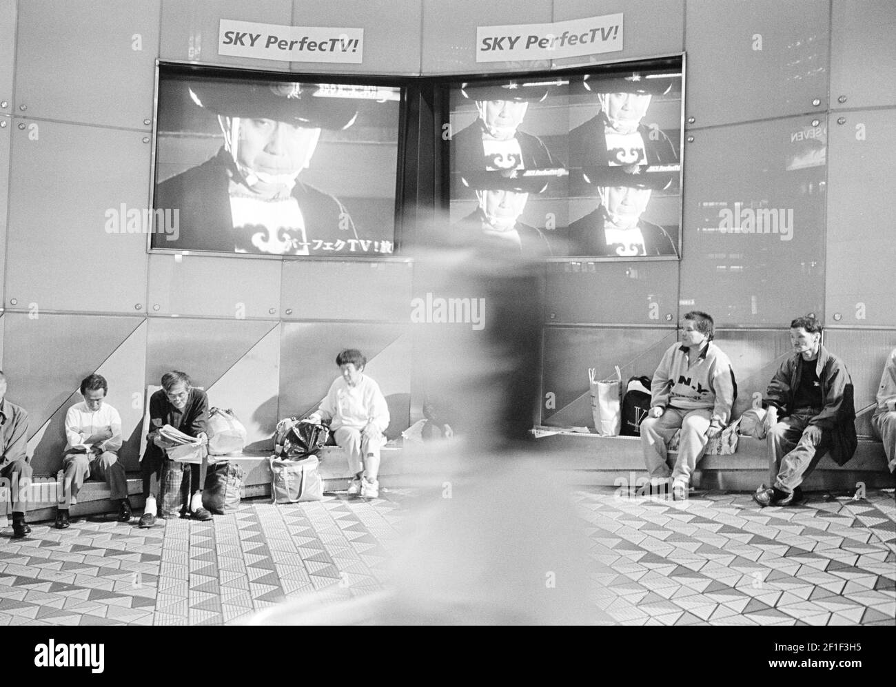 Groupe de personnes assis dans la salle d'attente regardant la télévision à la station de métro Tokyo au Japon . Banque D'Images