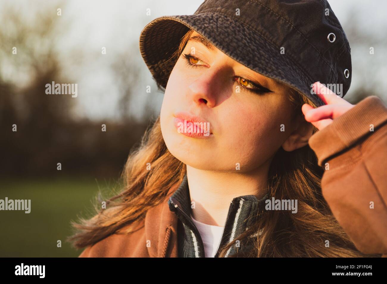 joli gros plan portrait d'une jolie jeune fille visage dans l'heure d'or du coucher du soleil portant un grand chapeau de disquette Banque D'Images