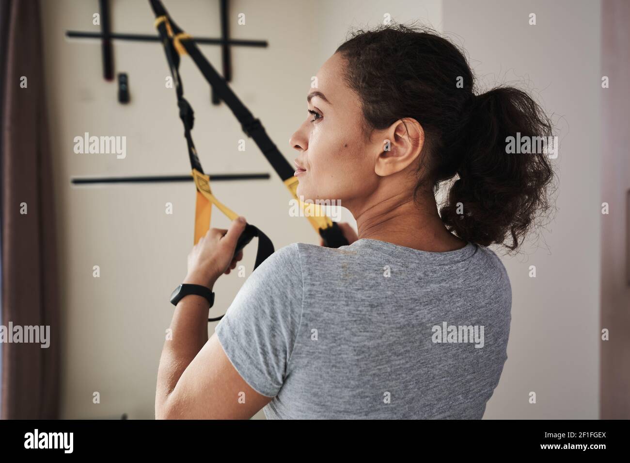 Gros plan sur le côté d'une jeune femme effectuant un entraînement fonctionnel avec des sangles de fitness. Style de vie sain, entraînement à l'intérieur, entraînement fonctionnel. Banque D'Images