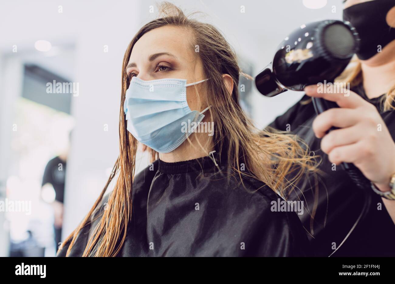 Coiffeur avec sèche-cheveux et client pendant les périodes de coronavirus Banque D'Images