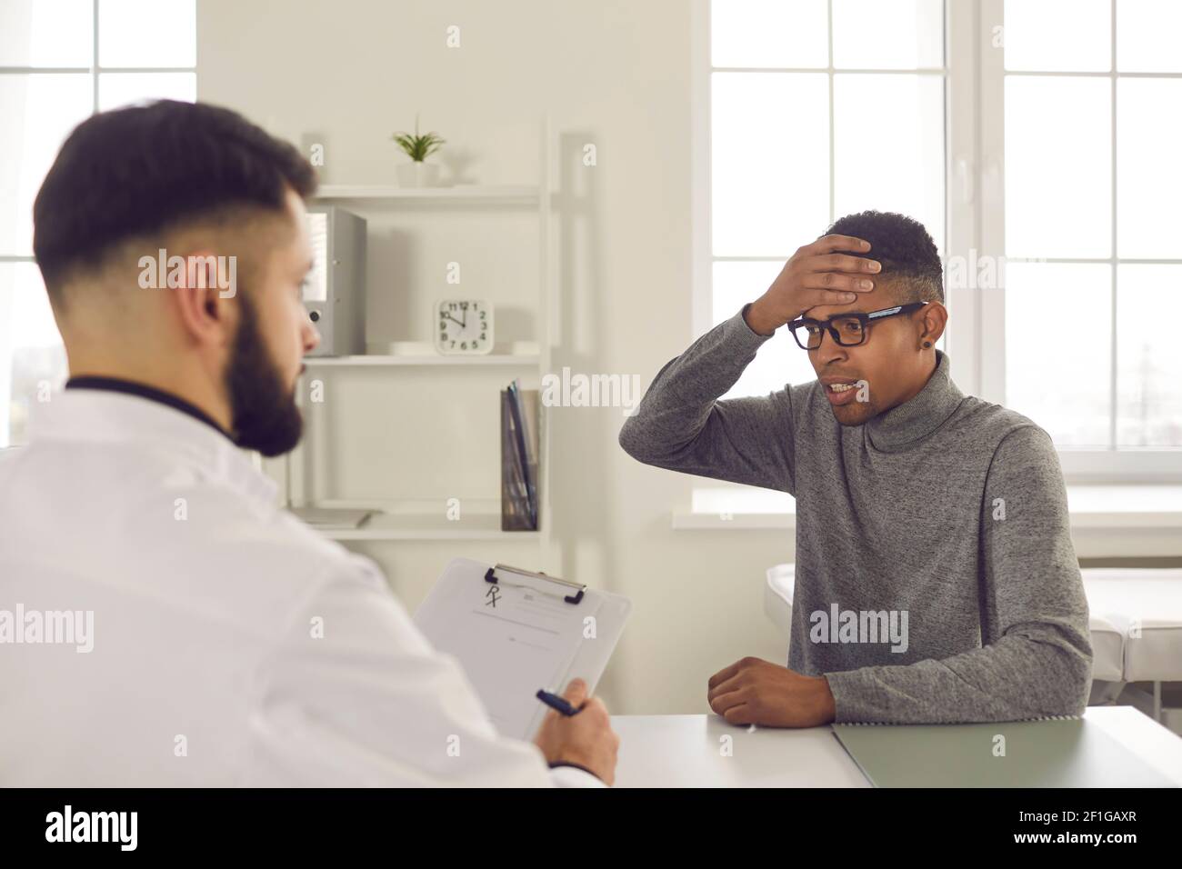 Jeune patient assis au bureau du médecin et se plaignant de constant maux de tête Banque D'Images