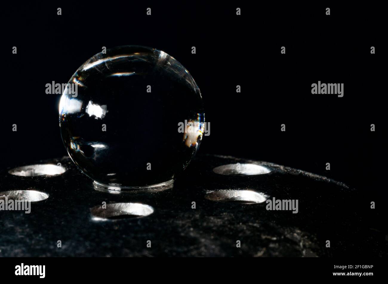 Sphère de verre en équilibre sur support métallique dans le noir arrière-plan Banque D'Images