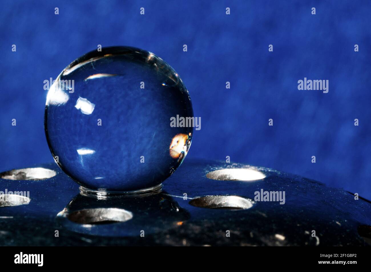 Sphère en cristal en équilibre sur support métallique sur fond bleu Banque D'Images