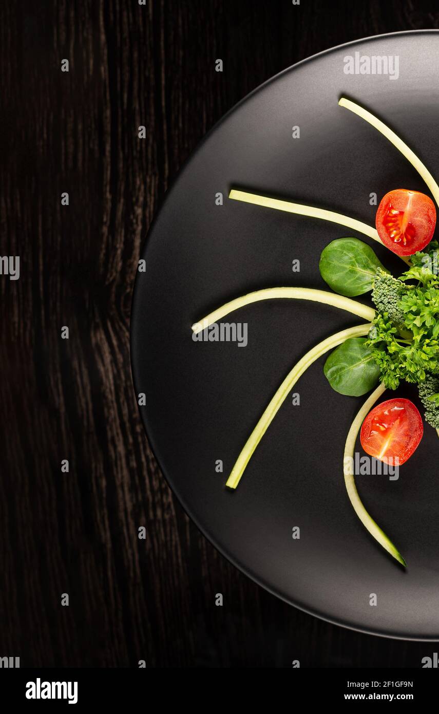 Les légumes en tranches sont sur une assiette noire sur un fond noir photographié. Vue de dessus. Tir vertical. Banque D'Images